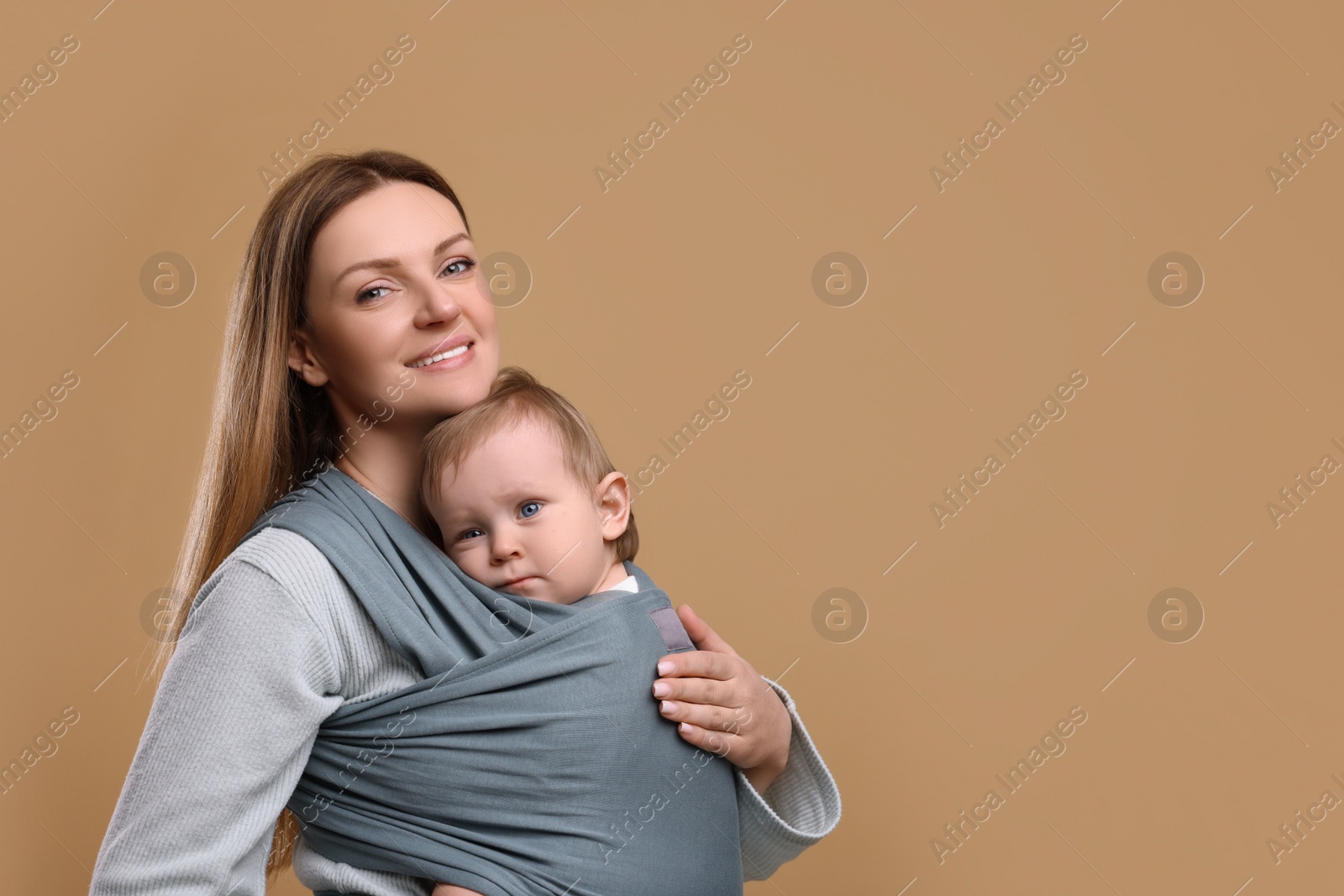 Photo of Mother holding her child in baby wrap on light brown background. Space for text