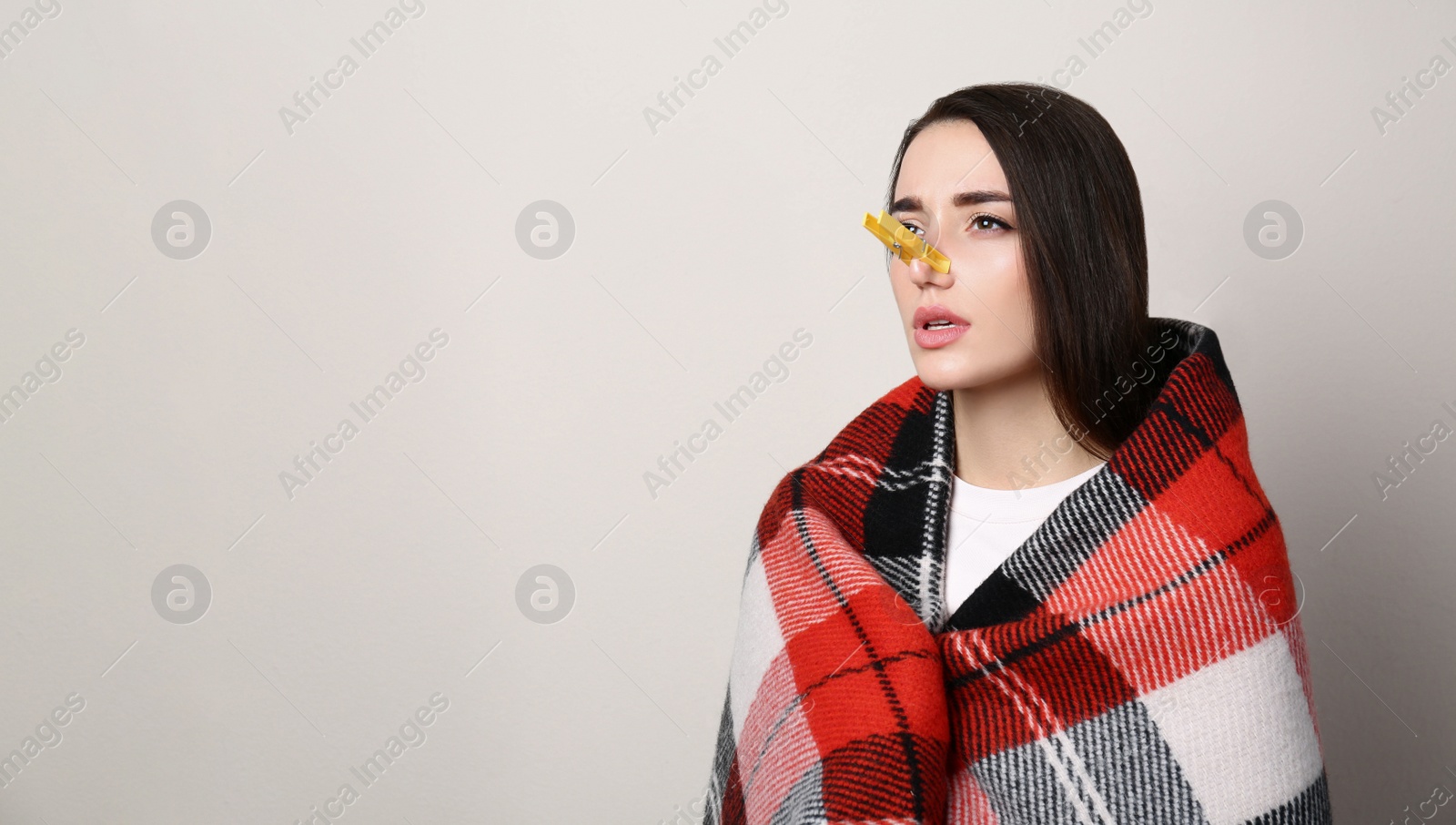 Photo of Young woman with clothespin on beige background, space for text. Runny nose concept