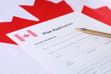 Photo of Immigration to Canada. Visa application form and pen on flag, closeup