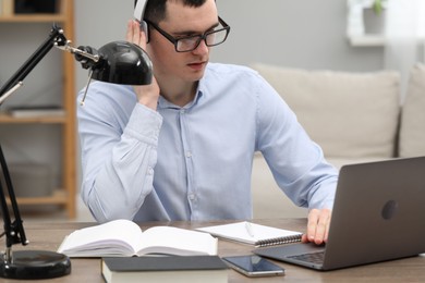 Photo of E-learning. Young man using laptop during online lesson at table indoors.