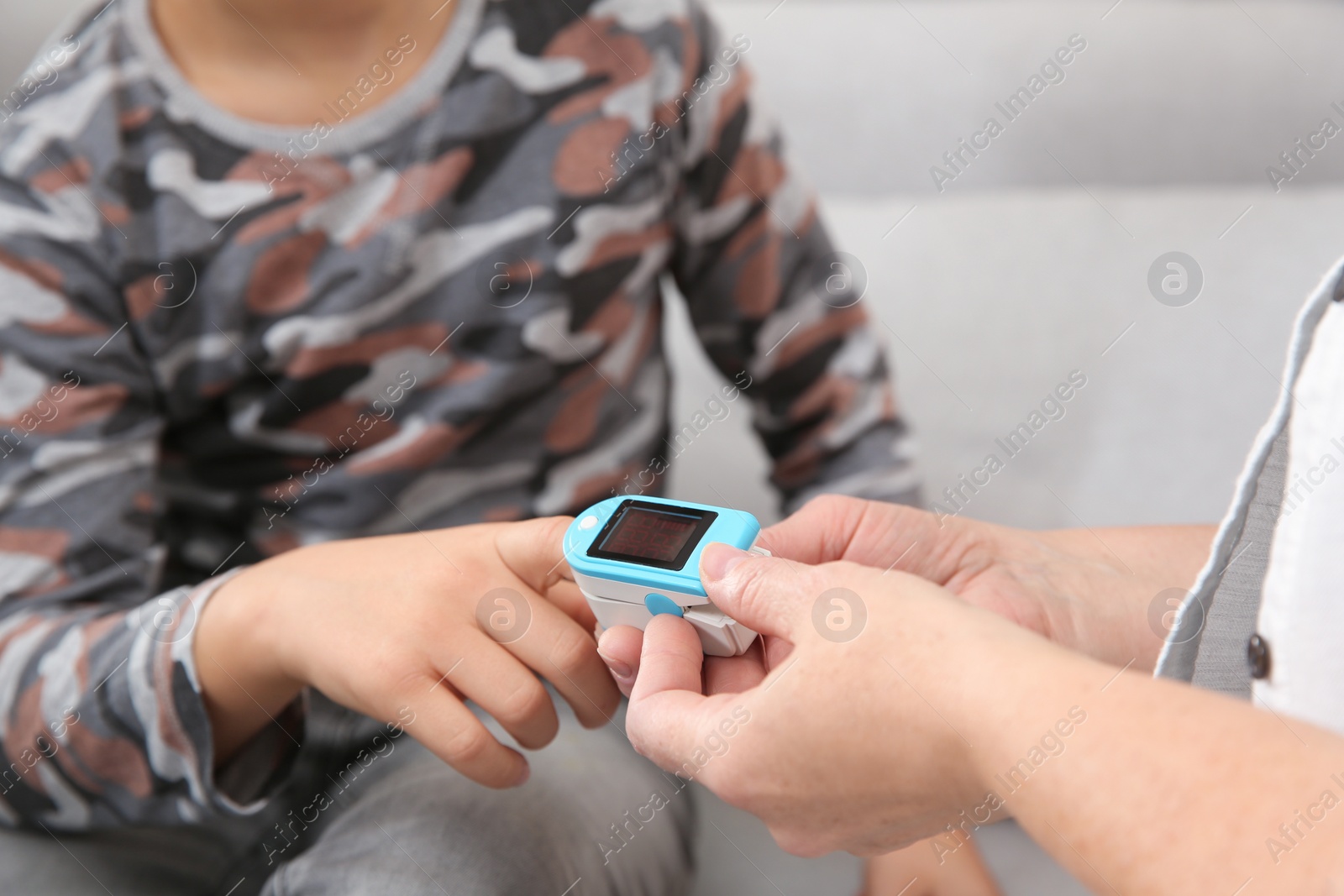 Photo of Mature woman checking little boy's pulse with medical device indoors, closeup