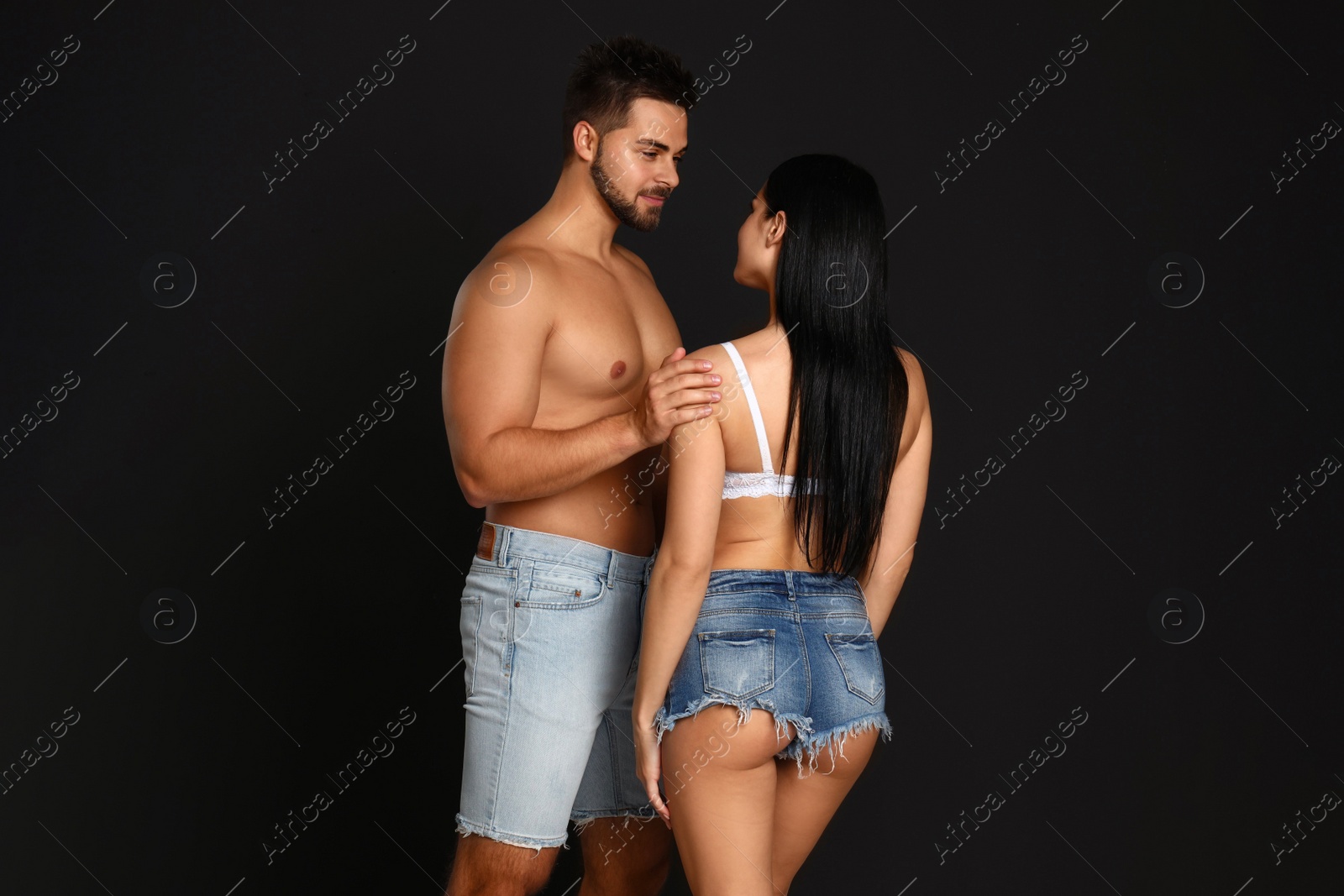 Photo of Young woman in underwear and denim shorts with her boyfriend on black background