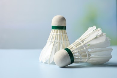 Photo of Feather badminton shuttlecocks on light blue table against blurred background, closeup. Space for text