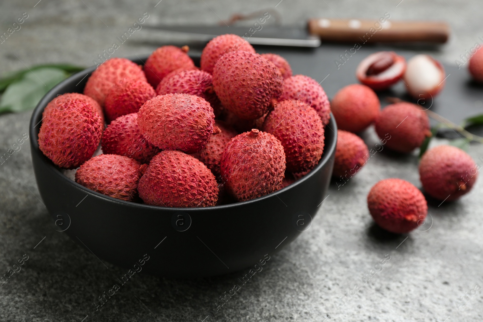 Photo of Fresh ripe lychee fruits in black ceramic bowl on grey table