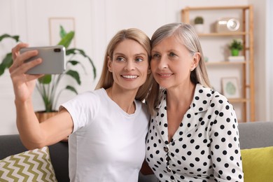 Photo of Happy daughter taking selfie with her mature mother at home