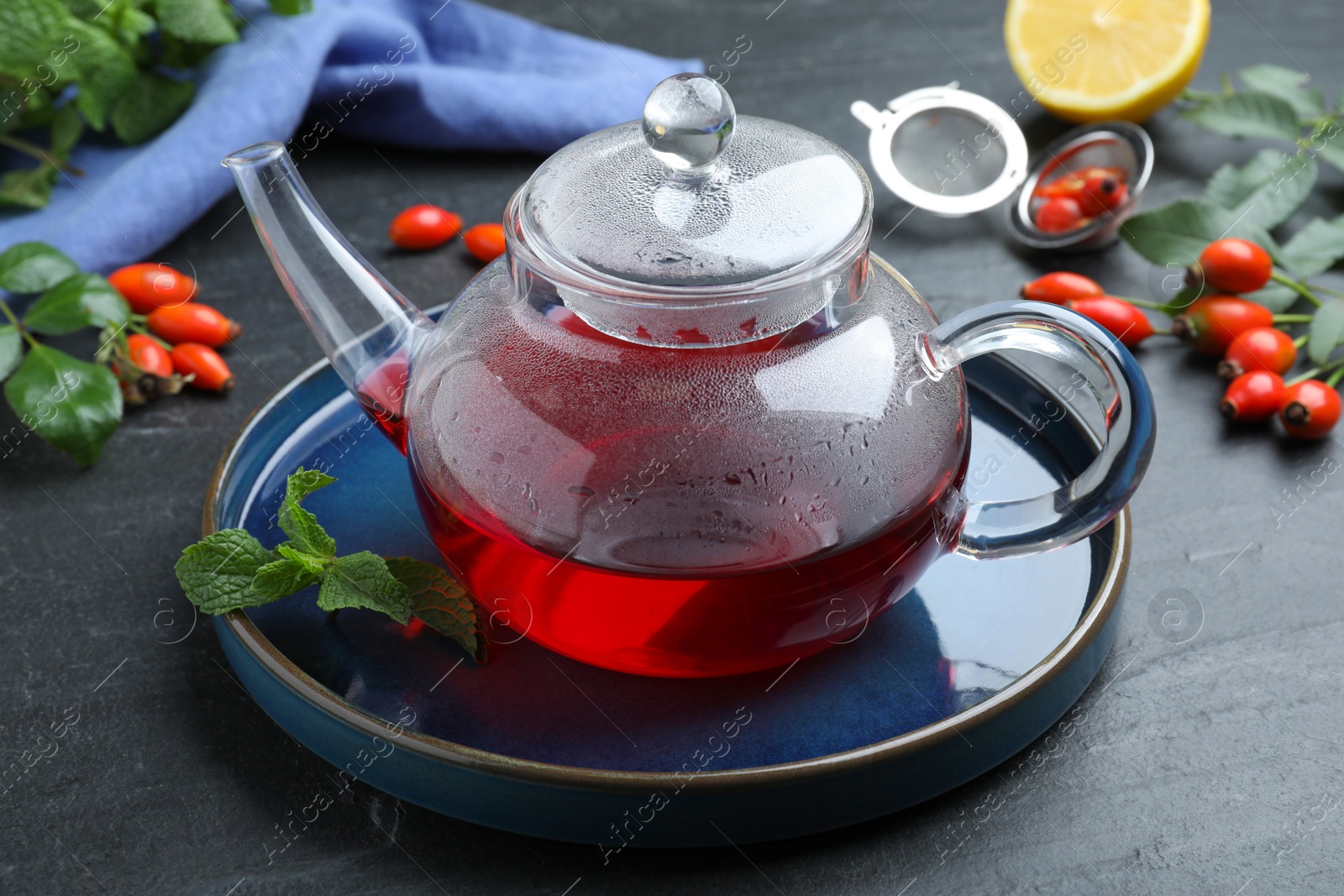Photo of Teapot with aromatic rose hip tea and fresh mint on black table