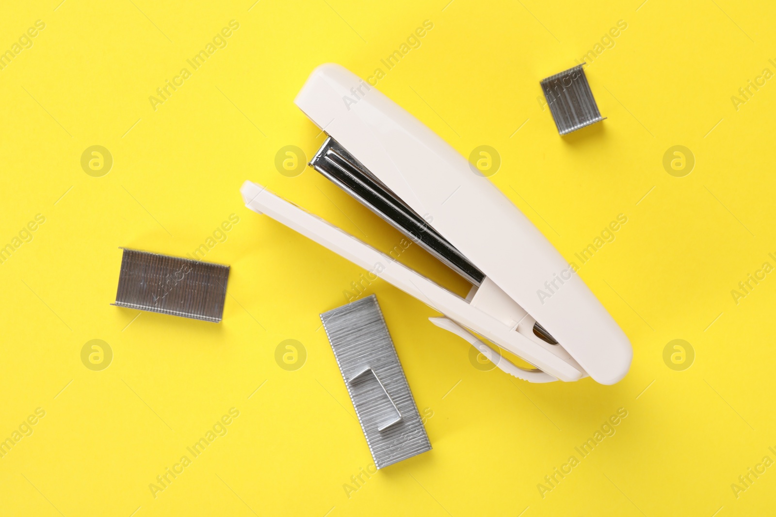 Photo of White stapler with staples on yellow background, flat lay