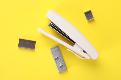 Photo of White stapler with staples on yellow background, flat lay