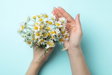 Photo of Woman holding chamomile bouquet on light background, top view