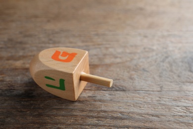 Photo of Hanukkah traditional dreidel on wooden table, closeup. Space for text