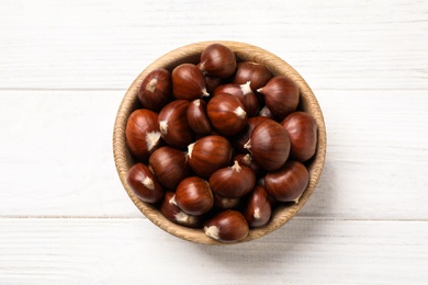 Photo of Fresh sweet edible chestnuts on white wooden table, top view