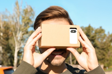 Photo of Young man using cardboard virtual reality headset outdoors