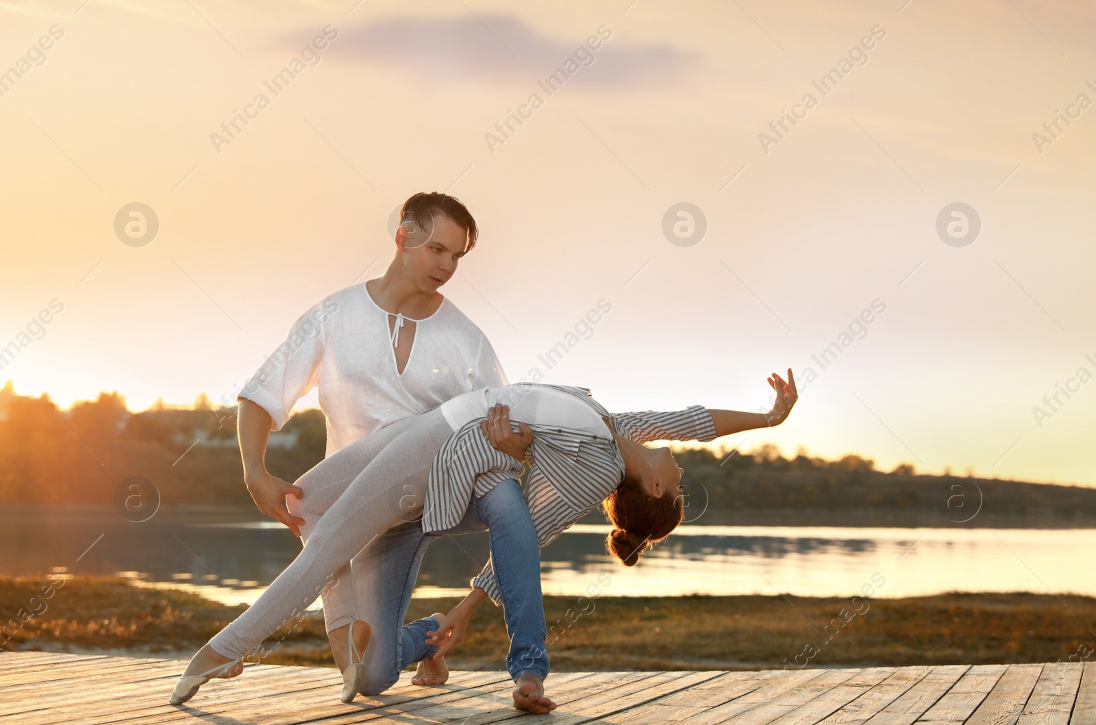 Photo of Beautiful young couple practicing dance moves near river at sunset