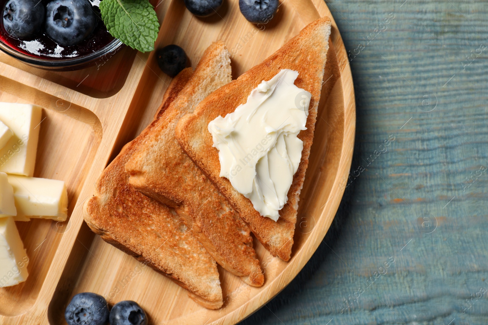 Photo of Tasty toasts with butter and blueberries on light blue wooden table, top view. Space for text