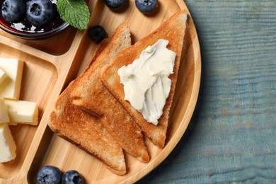 Tasty toasts with butter and blueberries on light blue wooden table, top view. Space for text