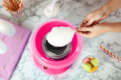 Woman making cotton candy using modern machine at table, above view