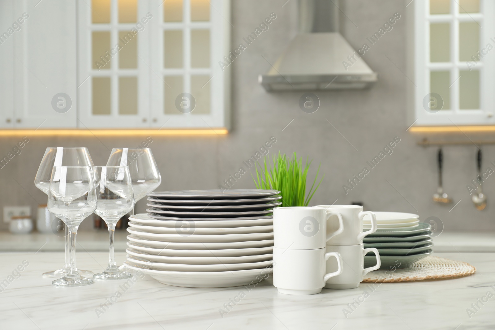 Photo of Clean plates, cups and glasses on white marble table in kitchen