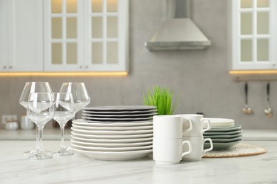 Clean plates, cups and glasses on white marble table in kitchen