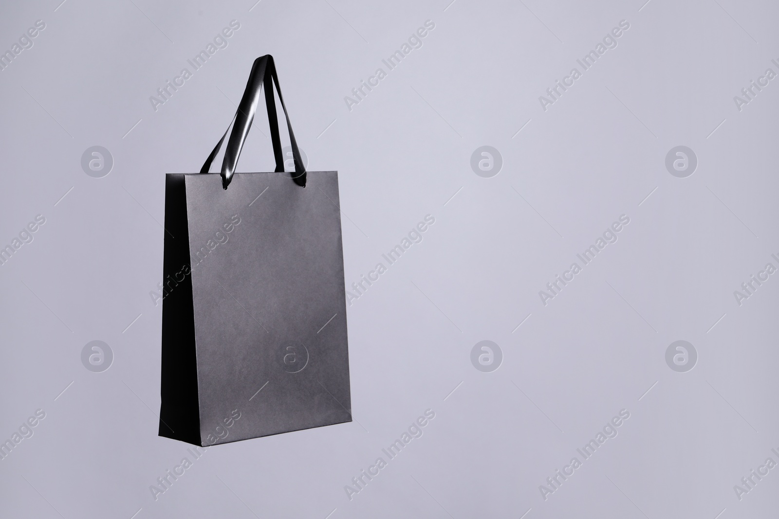 Photo of One black paper shopping bag on grey background. Space for text