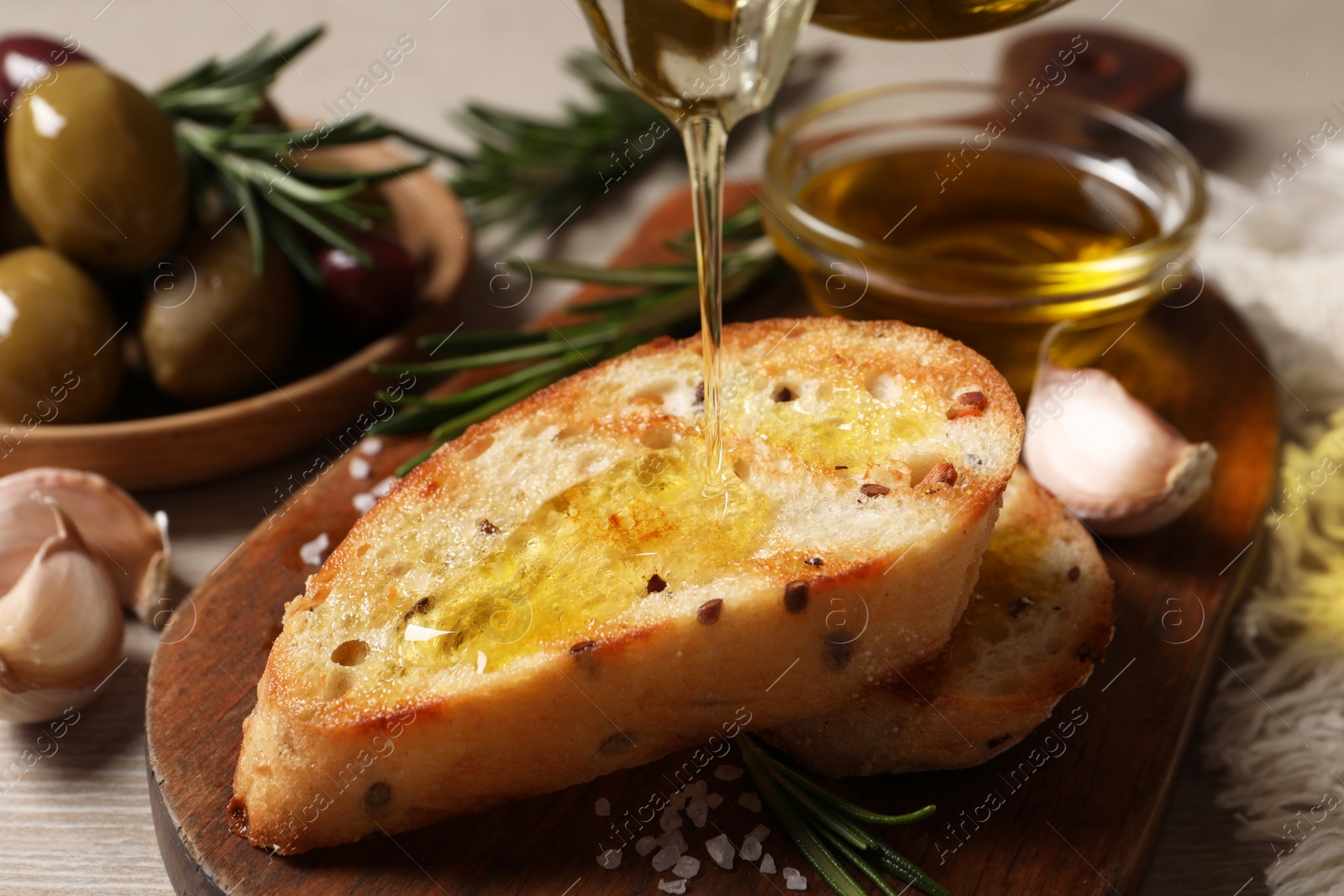 Photo of Pouring oil onto slice of toasted bread on wooden board, closeup