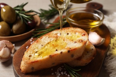 Photo of Pouring oil onto slice of toasted bread on wooden board, closeup