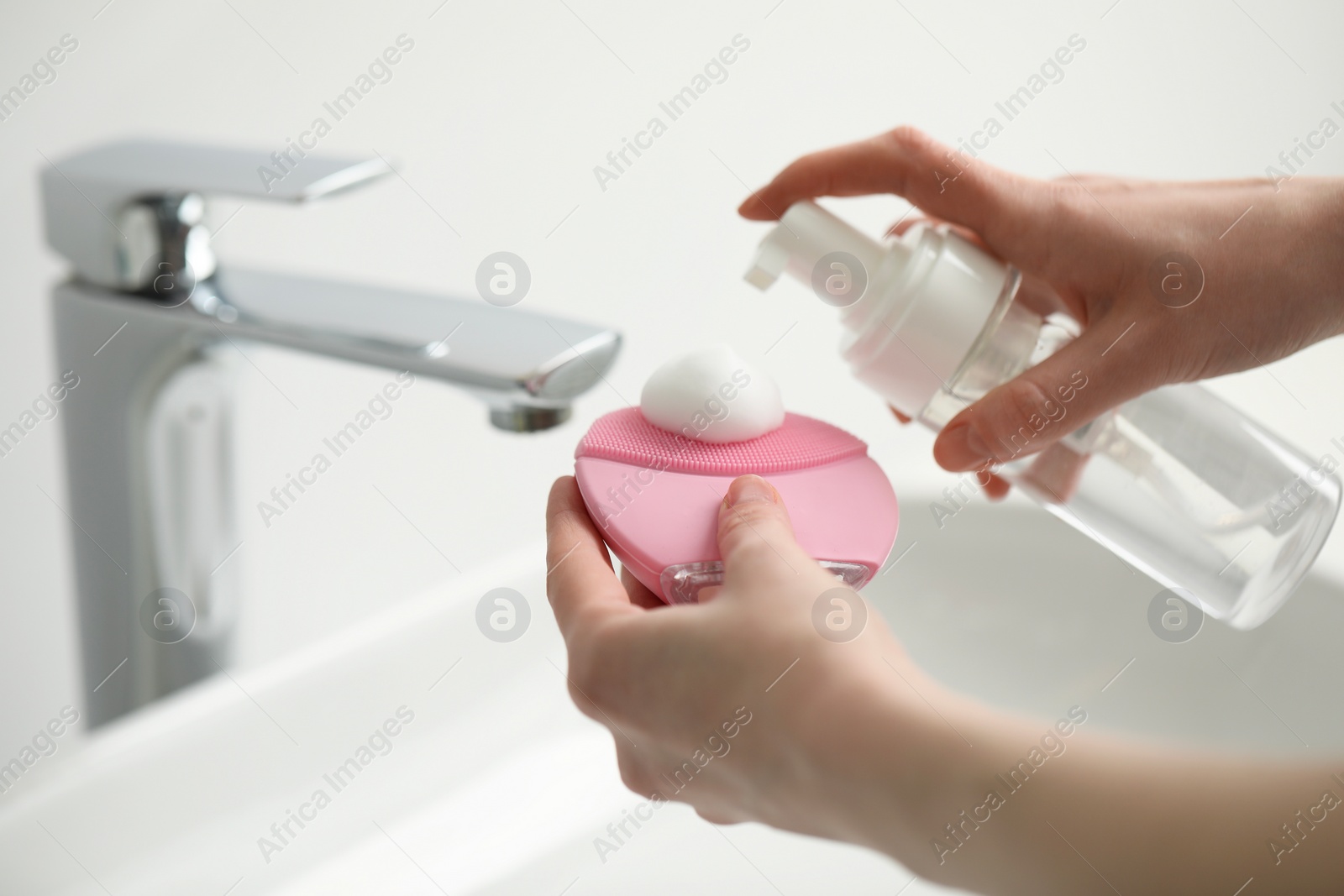 Photo of Washing face. Woman applying cleansing foam onto brush above sink in bathroom, closeup