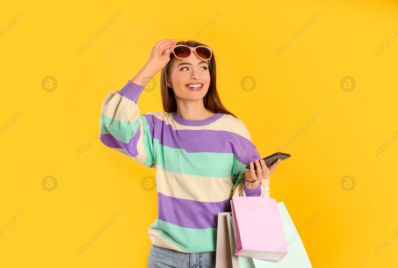 Photo of Happy young woman with shopping bags and smartphone on yellow background. Big sale