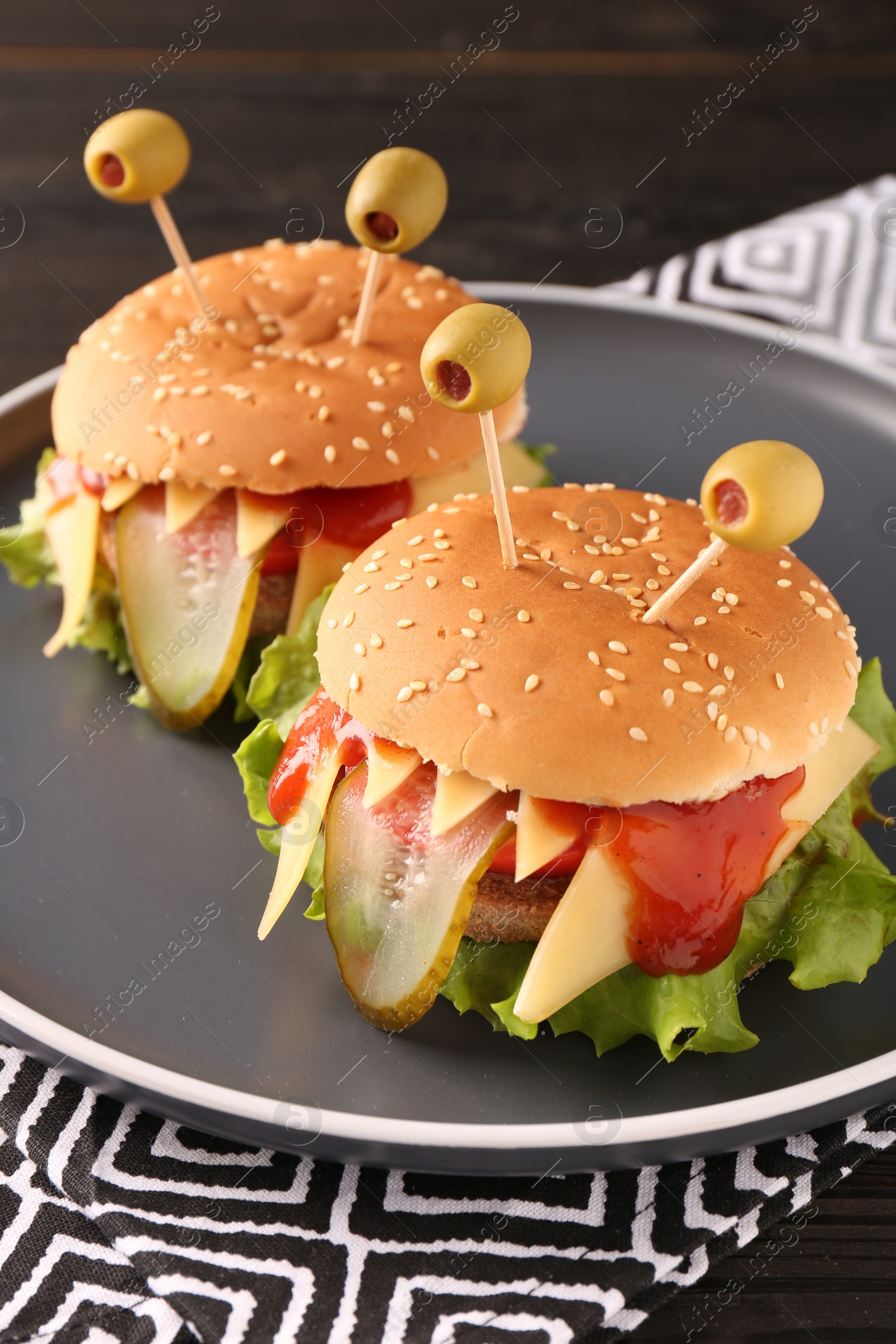 Photo of Cute monster burgers on table, closeup. Halloween party food