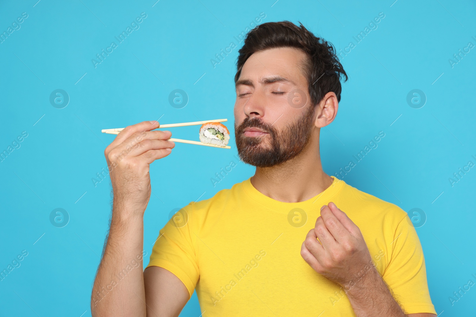 Photo of Emotional man holding sushi roll with chopsticks on light blue background