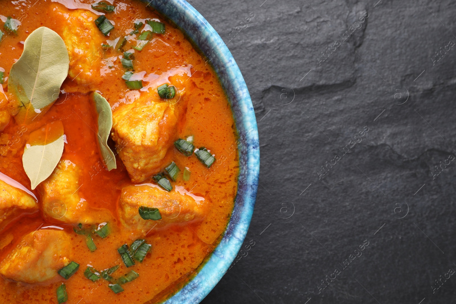 Photo of Bowl of delicious chicken curry on black table, top view. Space for text