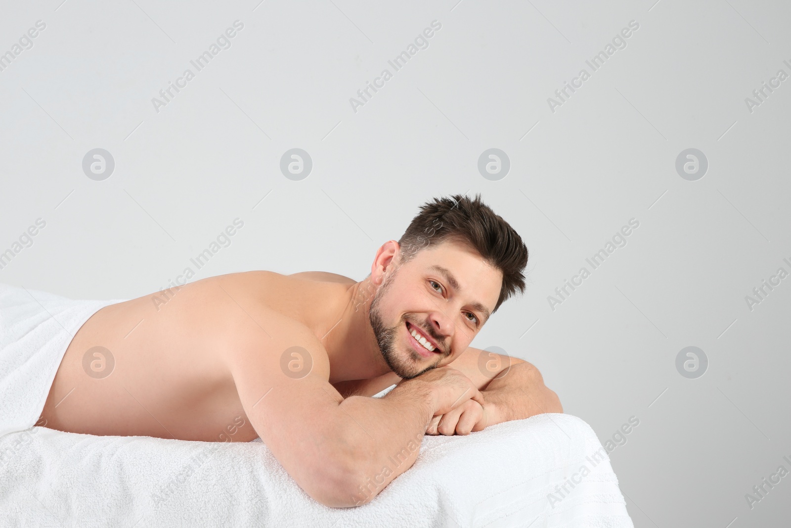 Photo of Handsome man relaxing on massage table against white background. Spa service