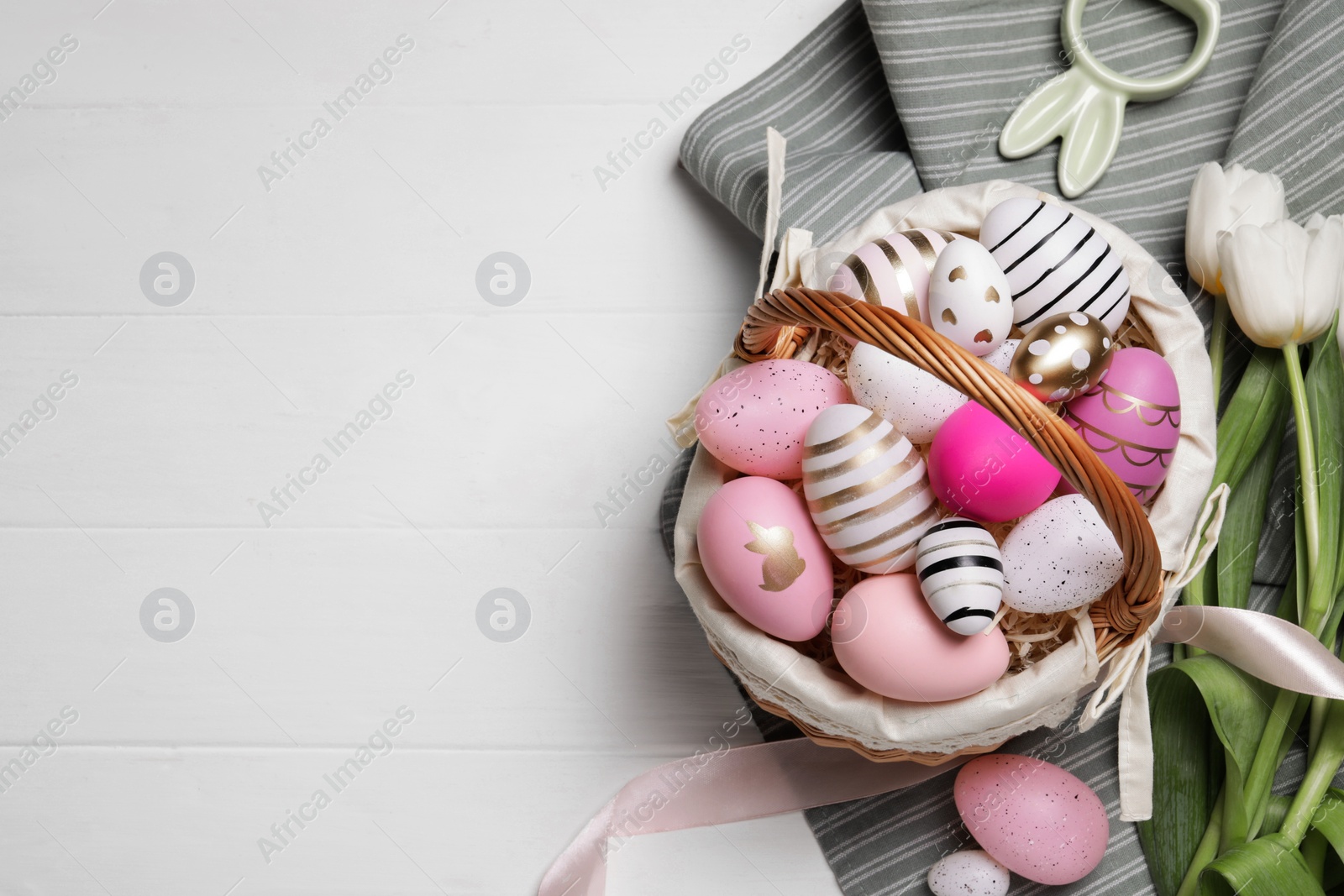 Photo of Flat lay composition with Easter eggs in basket and tulips on white wooden table. Space for text