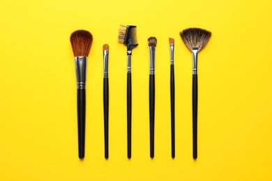 Photo of Set of makeup brushes on yellow background, flat lay