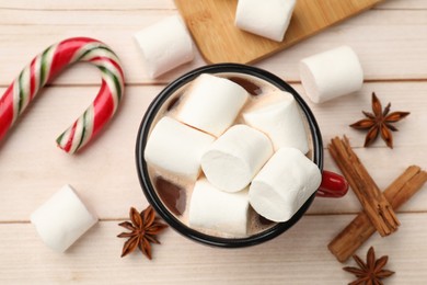 Photo of Tasty hot chocolate with marshmallows, candy cane and spices on light wooden table, flat lay