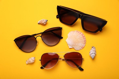 Stylish sunglasses and seashells on yellow background, flat lay