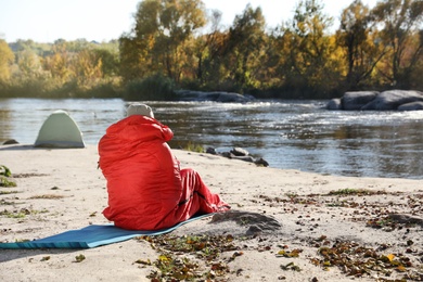 Photo of Male camper sitting in sleeping bag on wild beach. Space for text