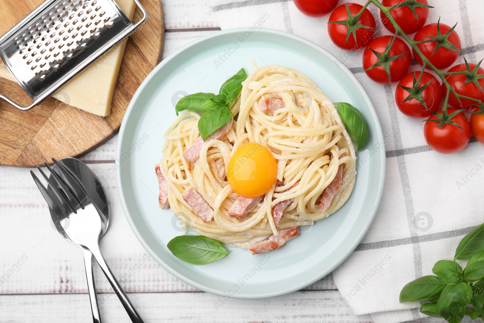 Photo of Delicious pasta Carbonara with egg yolk served on white wooden table, flat lay