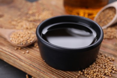 Photo of Bowl of natural oil and mustard seeds on wooden board, closeup