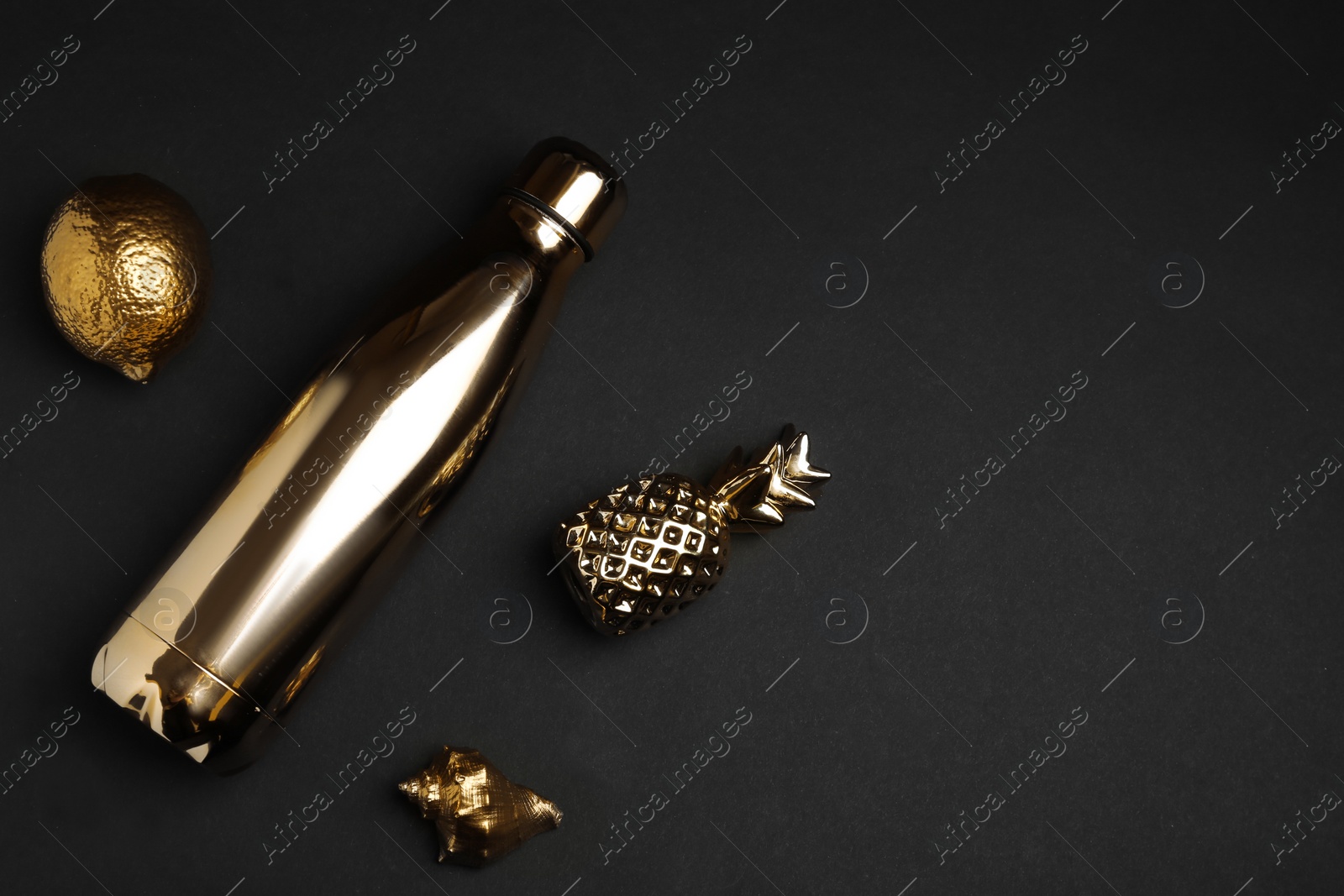 Photo of Flat lay composition with gold bottle, decorative pineapple, lemon and seashell on black background. Space for text