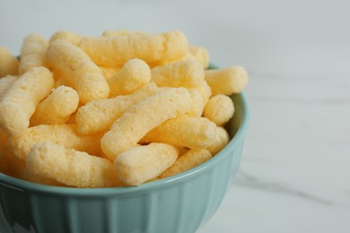 Bowl of delicious crispy corn sticks on white marble table, closeup