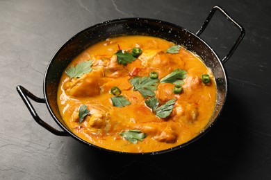 Photo of Tasty chicken curry with parsley and pepper on black textured table