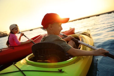 Photo of Happy children kayaking on river at sunset. Summer camp activity