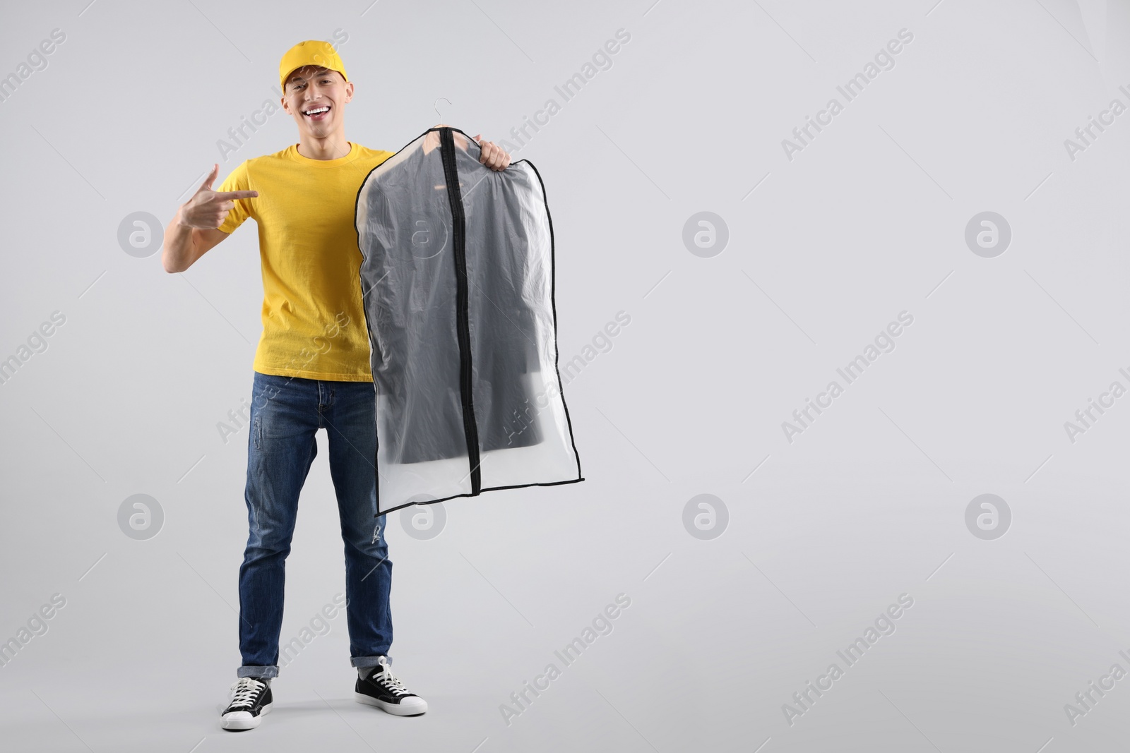 Photo of Dry-cleaning delivery. Happy courier holding garment cover with clothes on light grey background, space for text