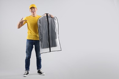 Dry-cleaning delivery. Happy courier holding garment cover with clothes on light grey background, space for text