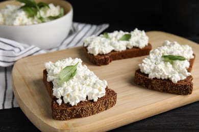 Photo of Bread with cottage cheese and basil on black wooden table, closeup