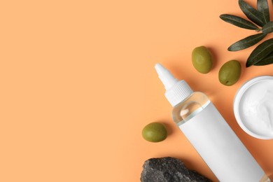 Flat lay composition with different cosmetic products and olives on pale orange background. Space for text