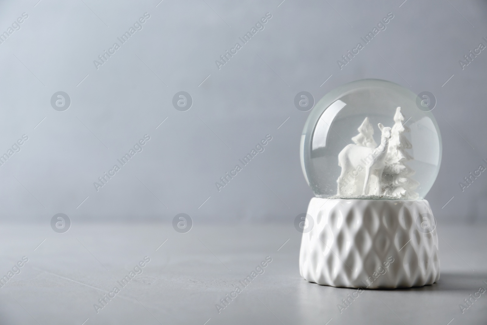 Photo of Snow globe with deer and trees on grey table, space for text. Christmas season