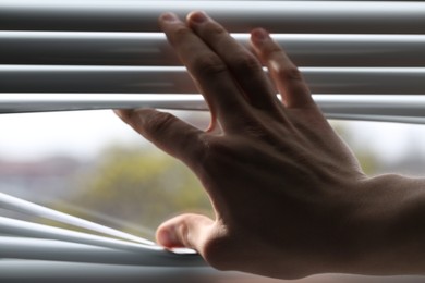 Photo of Man separating slats of white blinds indoors, closeup