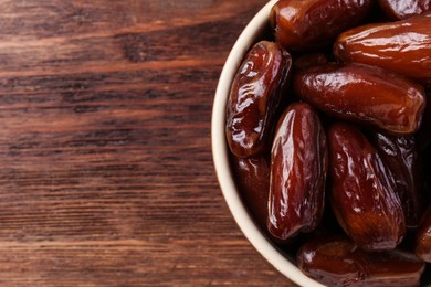 Photo of Top view of sweet dried dates in bowl on wooden background, closeup. Space for text