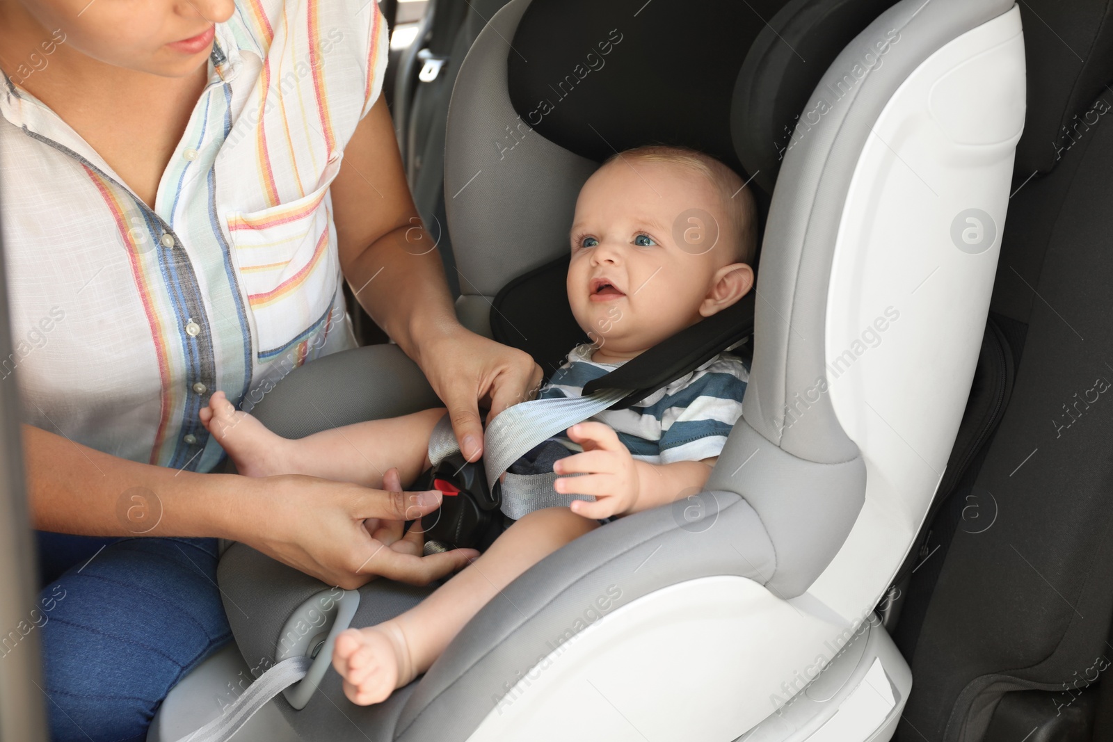 Photo of Mother fastening baby to child safety seat inside of car